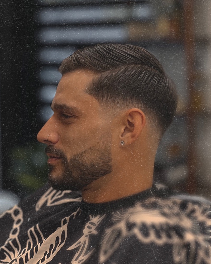 Low skin fade with a slicked side part and beard line-up, side profile